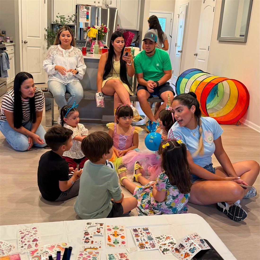 Host sitting on the floor with a circle of children while parents watch