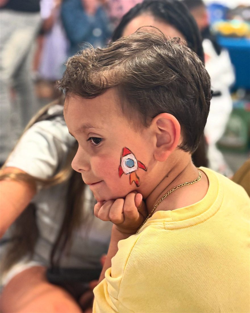 Boy in a yellow shirt with a red rocket painted on his cheek