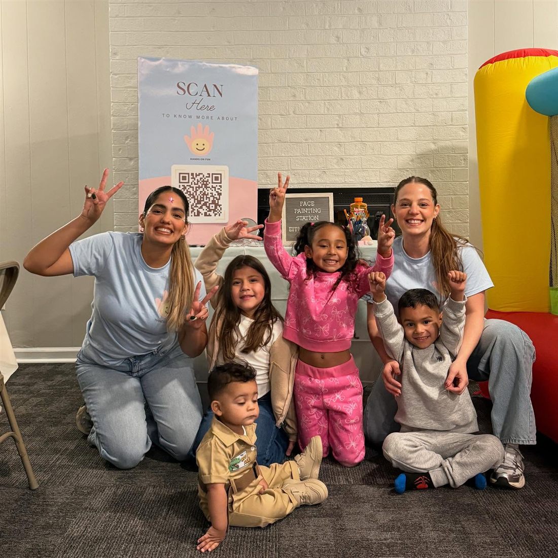 Two Hands On Fun hosts in light blue shirts posing with four smiling children at a first birthday party